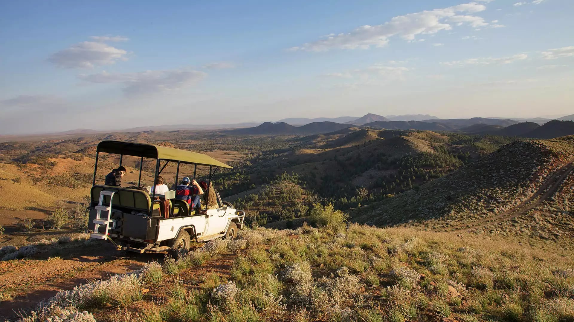 A white open-air safari vehicle parked on a ridge overlooking a vast valley in the Australian outback.
