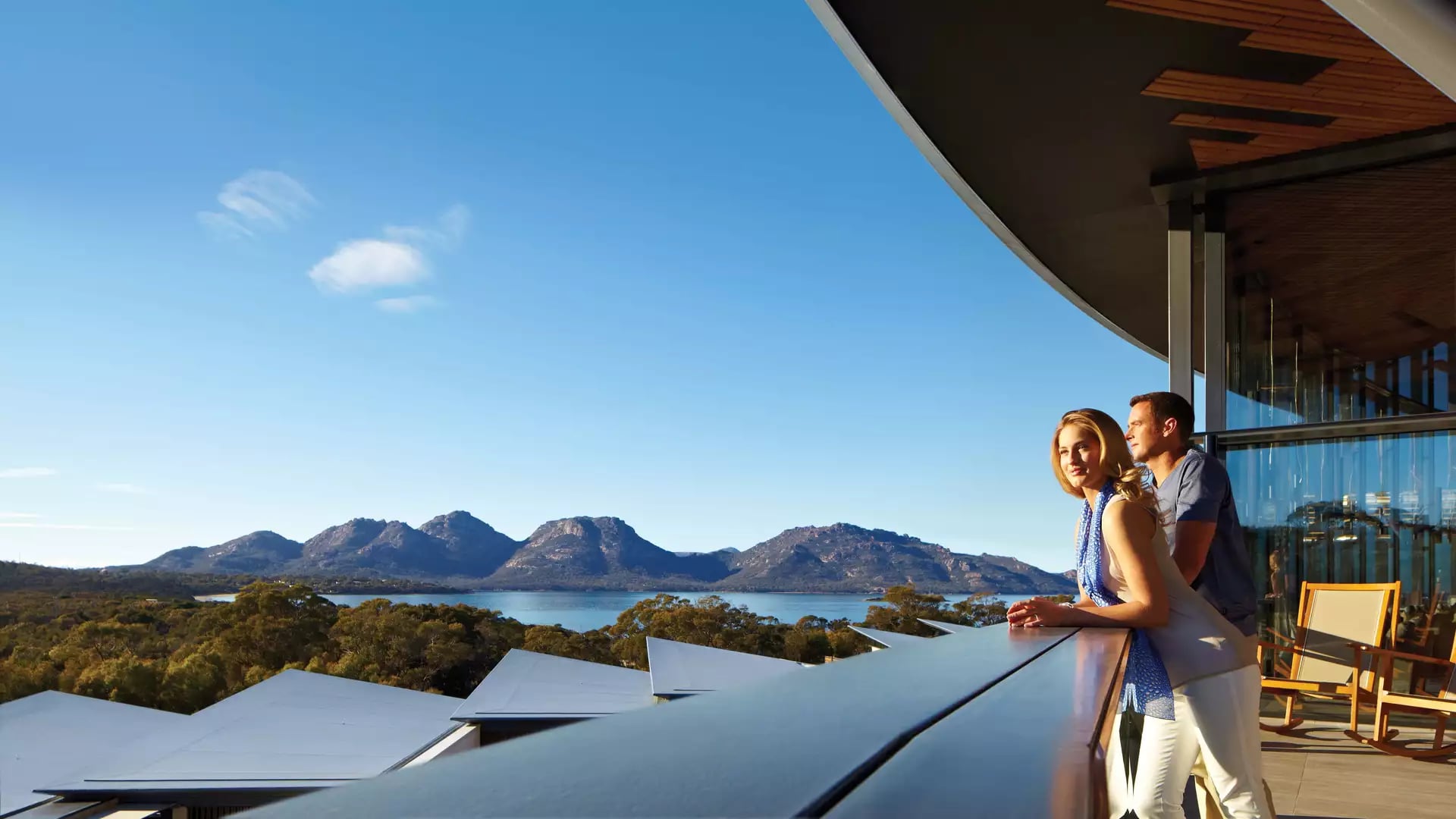 Guests relaxing on the expansive outdoor timber deck of Saffire Freycinet, offering a premier vantage point over the Great Oyster Bay and the Hazards mountain range.