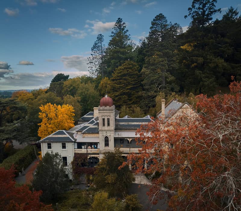High-angle view of a historic white convent building surrounded by autumn trees in Daylesford.