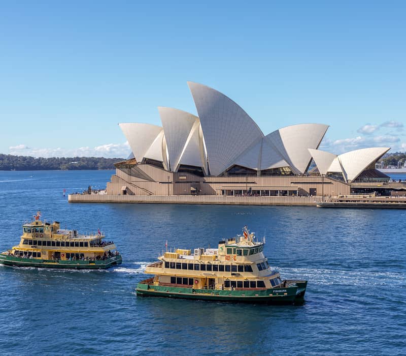 Sydney Opera House and Sydney ferries on the harbour under a clear blue sky.