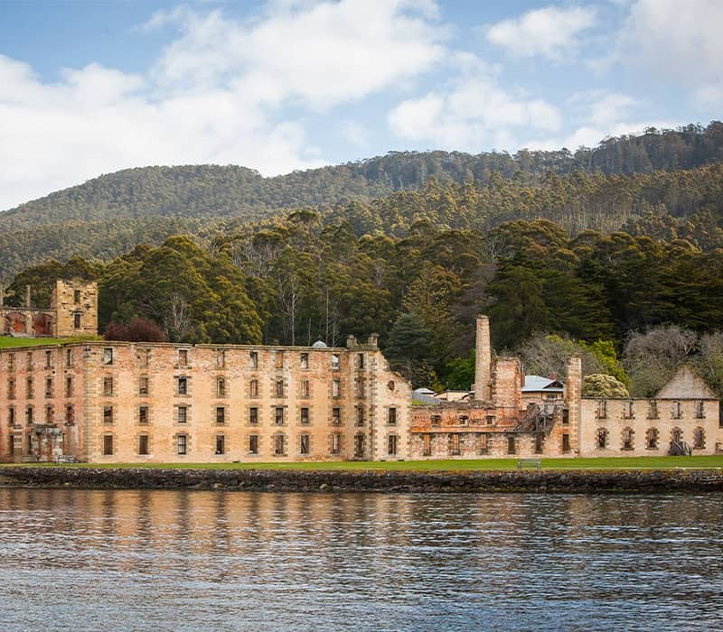 Port Arthur historic site with sandstone buildings and lush forest backdrop.
