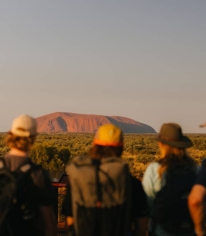 Rear view of a group of hikers looking out towards Uluru under a clear sky in the Northern Territory.