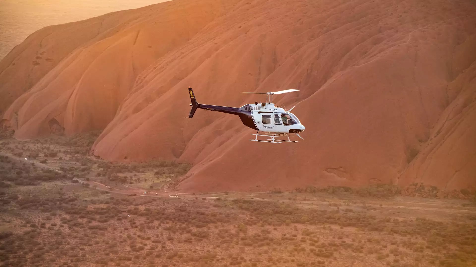 A scenic helicopter flying past the red rock face of Uluru during a morning tour in the Northern Territory.