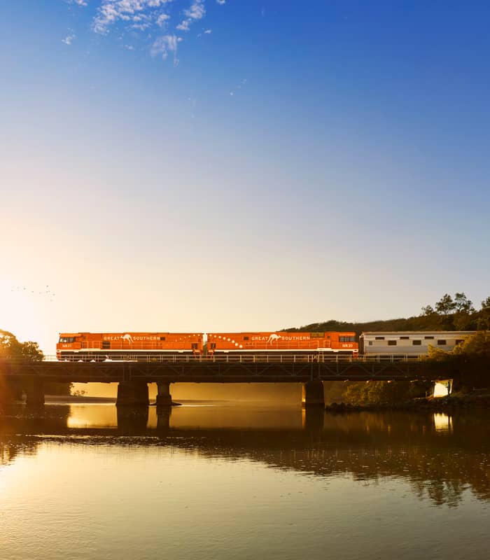 A train crossing a bridge at sunset with its reflection in the water.