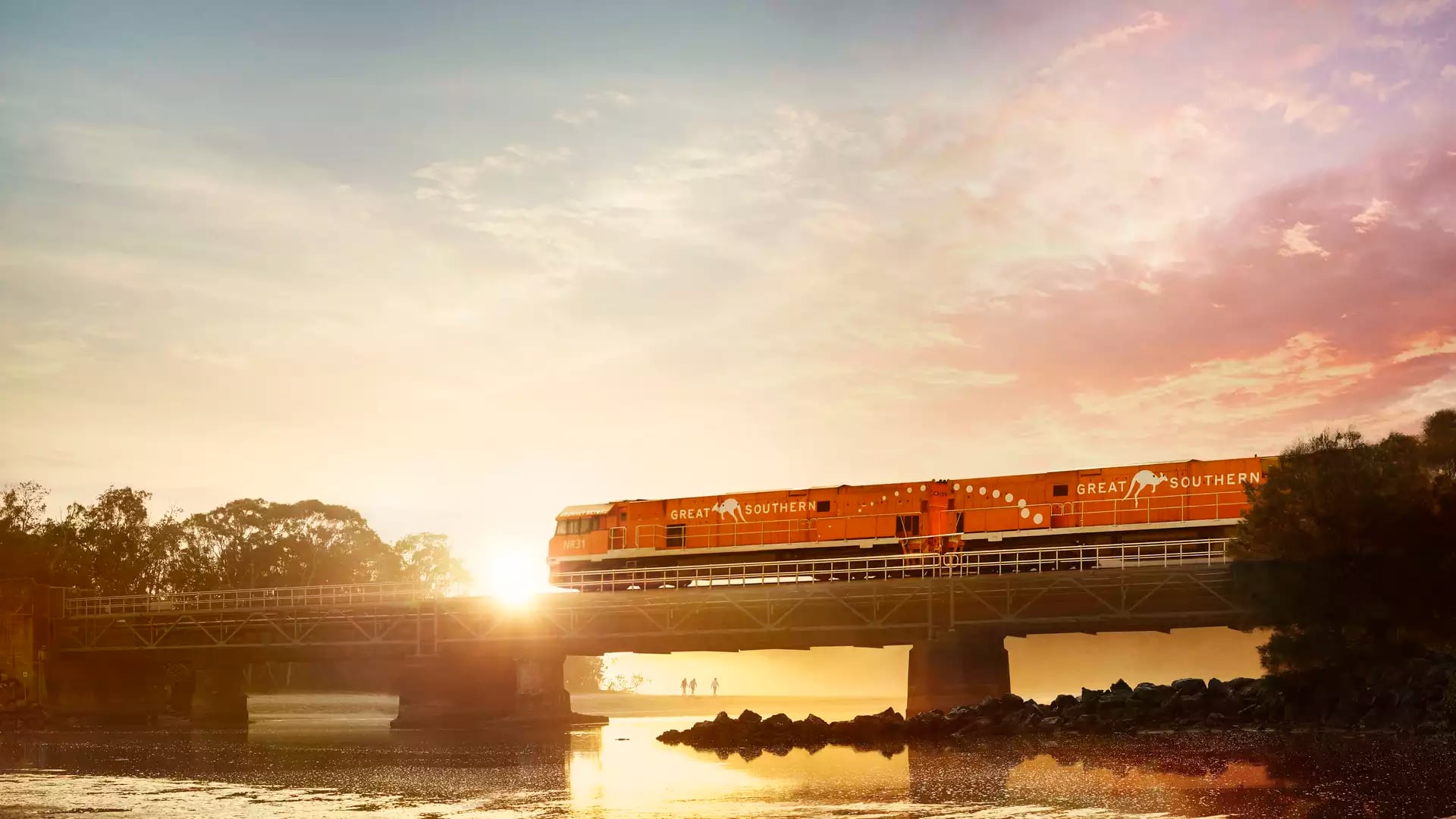 A train on a bridge at sunrise with a vibrant pink and orange sky.
