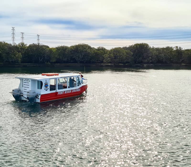 A red and white tour boat cruising on the shimmering Port River under a bright sky.